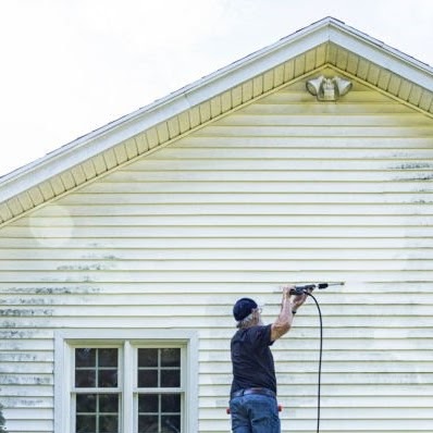 Real life, real person DIY senior man is balanced near the top of a ladder while cleaning the vinyl clapboard siding on his house with high pressure cleaning power wash equipment. Very satisfying to see such clear progress as he methodically moves the spray nozzle back and forth across the grungy grimy surface!