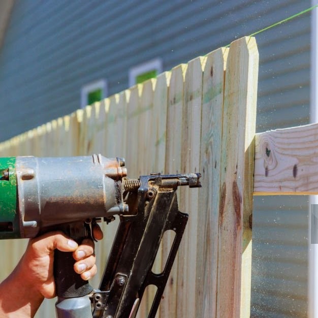 Man builds sections of nailing a wooden fence around his yard out planks using air nail gun